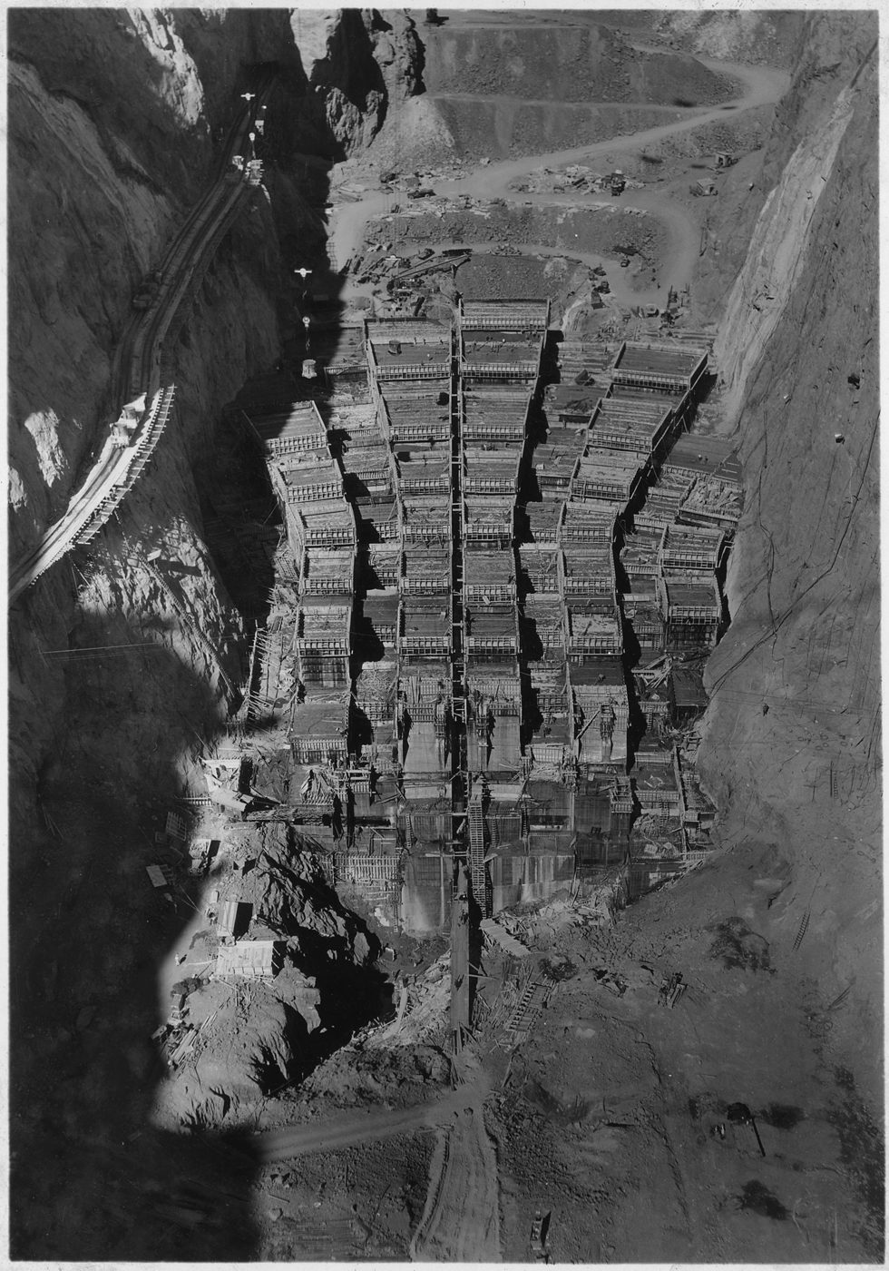 Hoover Dam under construction, interlocking concrete columns rising in Black Canyon with cableways strung across the gorge.