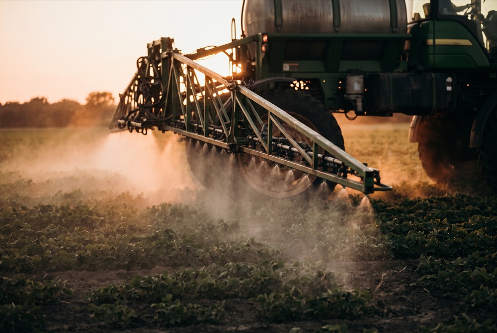 A green precision sprayer with a wide boom sweeping a field at golden hour